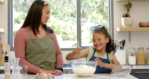 Mother and daughter whisking batter together in bright sunlit kitchen aprons joyful baking