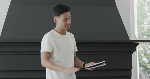 Young Man Holding Notebook Indoors by Fireplace in Casual Style