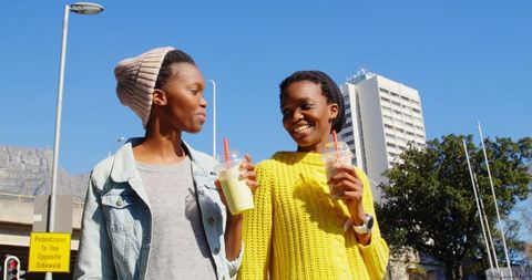Cheerful Twin Sisters Walking with Smoothies in City