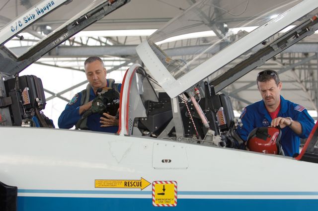 NASA astronauts are seen preparing for a flight in a T-38 trainer jet at Ellington Field. Astronauts Scott D. Altman and Michael J. Massimino are checking equipment and discussing the mission. The image can be used to illustrate articles on astronaut training, space missions, or aerospace technologies.