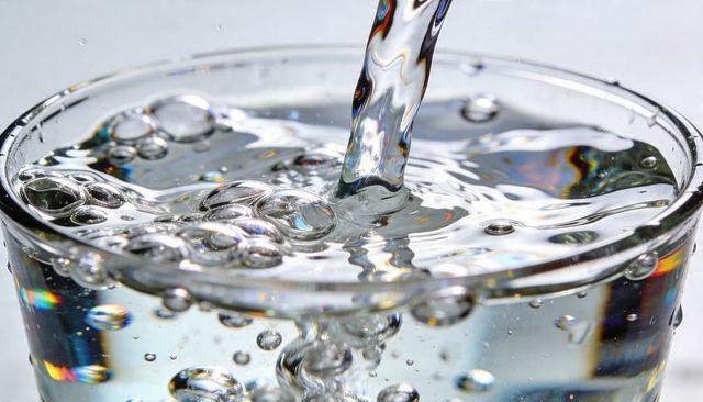 Pouring crystal-clear water into glass creating bubbles, ripples and rainbow refractions