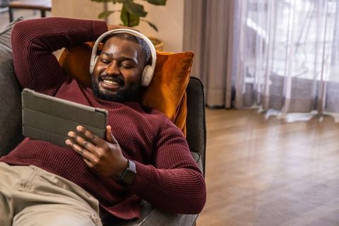 Relaxing african american man listening with headphones and using tablet on sofa