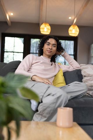 Relaxed non-binary person lounging on cozy gray sofa with warm home lighting