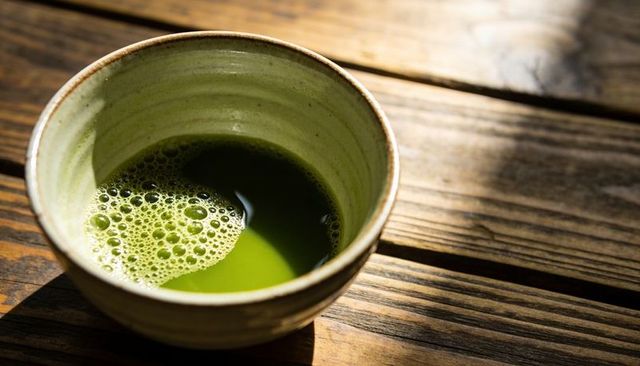 Sunlit ceramic matcha bowl with froth on rustic wooden table, close-up tea ritual