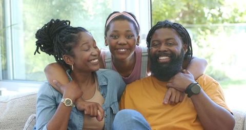 Smiling african family relaxing on couch with teen daughter hugging parents showing watch
