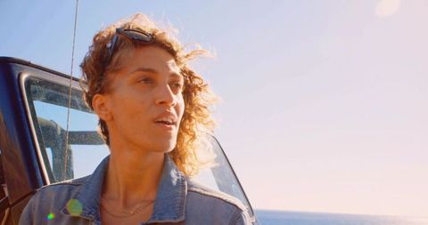 Woman enjoying sunset in denim jacket at coast with off-road vehicle