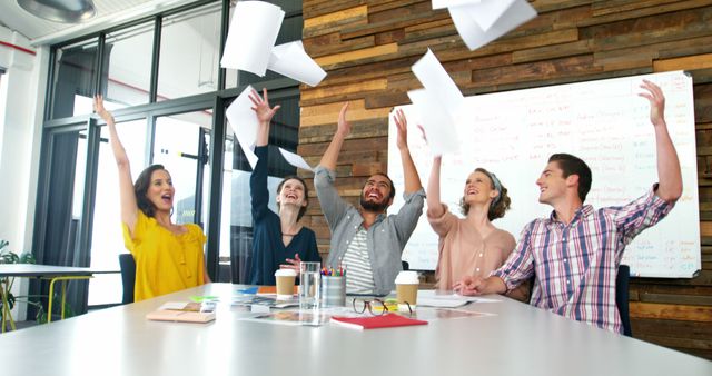 Diverse group of colleagues celebrating success by throwing papers in the air in a modern office. Ideal for themes of teamwork, achievement, business success, positive work environment, corporate celebrations, and office dynamics.