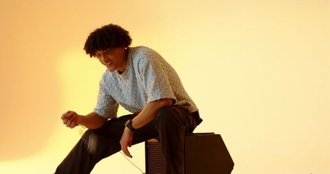 Man sitting on amplifier gripping guitar cable in cozy studio atmosphere