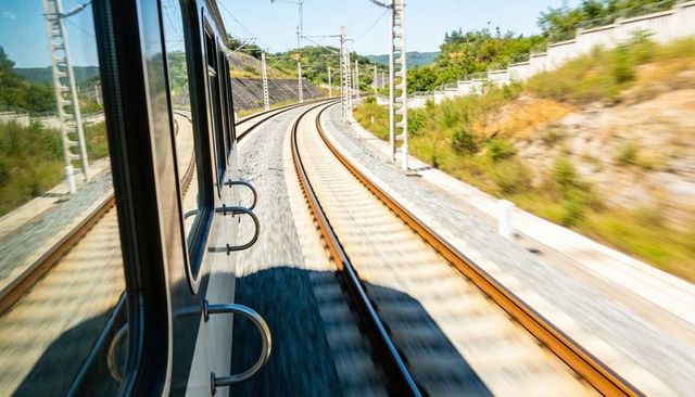 High-speed train passing curved electrified tracks, carriage side and motion reflections