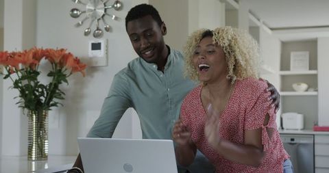 Joyful couple engaging with online content on laptop in kitchen