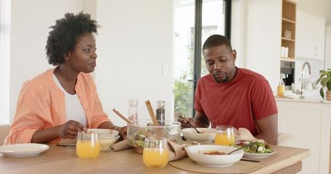African american couple sharing casual dinner at modern kitchen table with salad and juice