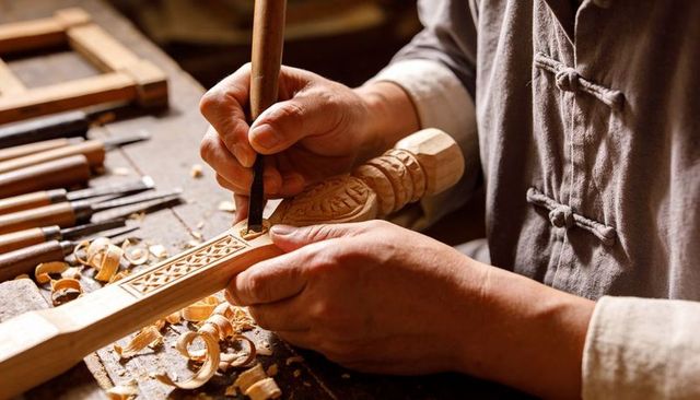 Master woodcarver carving intricate wooden relief with chisel, closeup hands and shavings