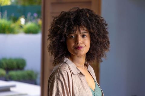 African american woman standing by doorway wearing beige shirt and green top