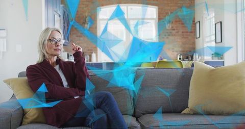 Senior woman sitting on sofa wearing cardigan and glasses with blue digital overlay