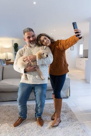 Couple taking cozy selfie while holding golden retriever puppy in bright modern living room