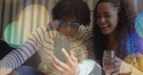 Smiling couple enjoying cozy lounge night, taking selfie with smartphone and sparkling drink