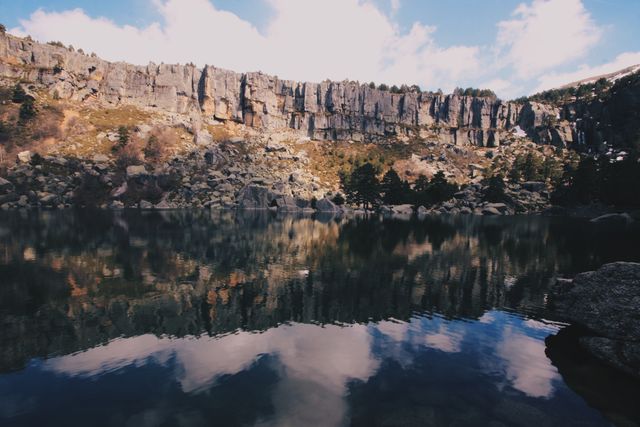 Stunning nature scene with calm lake reflecting rocky cliffs and sky. Ideal for travel blogs, outdoor adventure websites, nature conservation campaigns, desktop wallpapers, and relaxation imagery.
