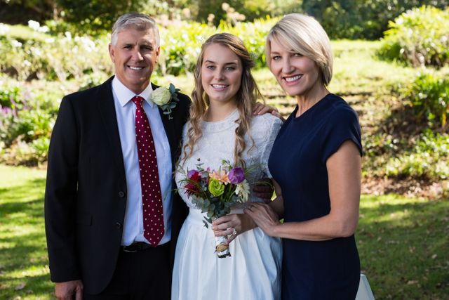 Portrait of bride standing with her parents in park