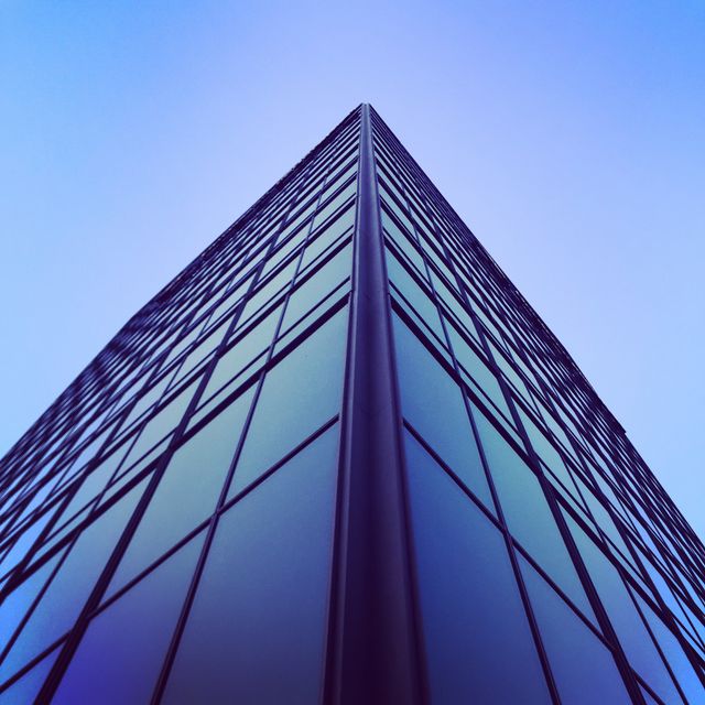 Low angle perspective highlighting modern glass office building reaching towards the sky. Glass facade reflecting skyline giving corporate urban aesthetic. Ideal for use in articles about urban architecture, corporate business environments, or illustrating metropolitan growth and development.