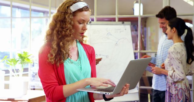 Female Entrepreneur Using Laptop in Office with Team in Background - Download Free Stock Images Pikwizard.com