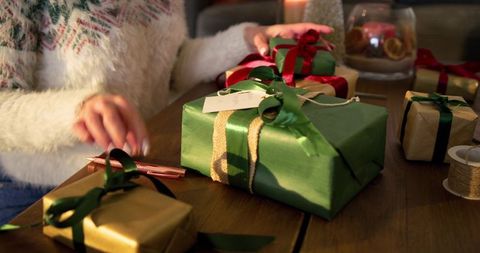 Wrapping Holiday Gifts with Burlap Ribbon and Satin Bow in Cozy Candlelit Table Scene