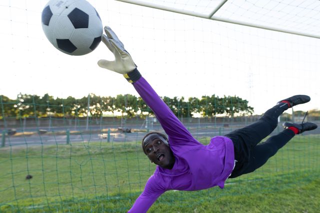 African american goalkeeper jumping and catching soccer ball in mid-air while defending goal. Copy space, net, match, unaltered, soccer, competition and sport concept.