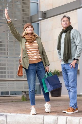 Mature couple hailing ride while holding shopping bags outside contemporary urban mall