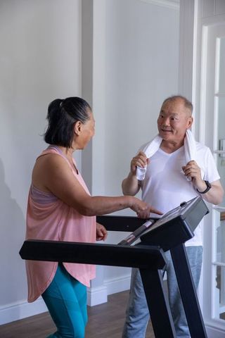 Senior chinese couple working out on treadmill at home sharing smile and guidance for active aging
