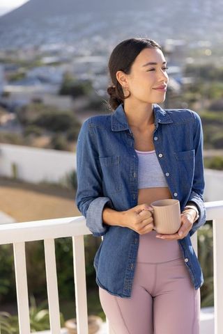 Young woman standing on balcony holding mug gazing at mountain view during morning relaxation