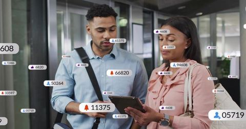 Coworkers discussing digital notifications while checking tablet in modern office corridor