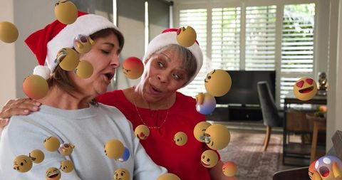 Singing duo wearing santa hats during virtual caroling with floating emoji spheres