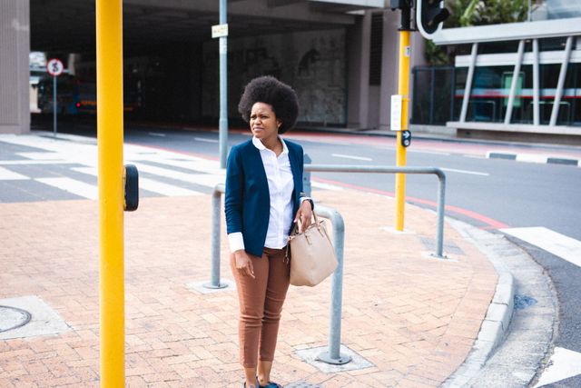 African american mid adult business woman looking away while standing on footpath by road in city. unaltered, formalwear, business person and city life.
