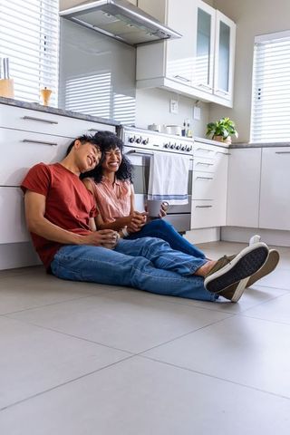 Couple relaxing on kitchen floor sharing coffee in sunlit minimalist kitchen