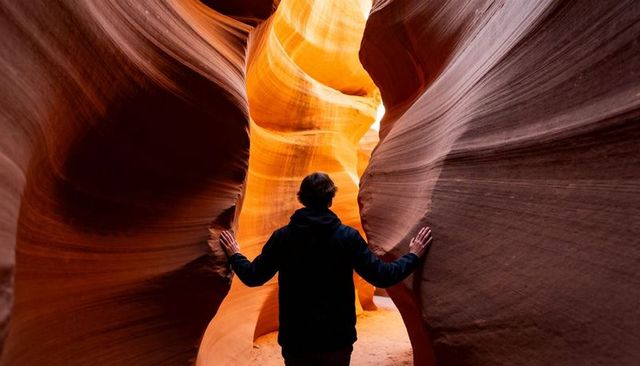 Exploring sunlit slot canyon with hands on sculpted sandstone walls, silhouette hike