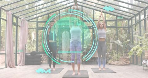 Three women practicing yoga in glass greenhouse studio with cyan digital HUD overlay, yoga mats and 