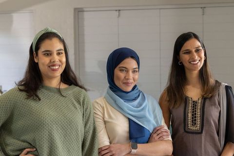 Diverse women standing together smiling, wearing hijab, headband and ethnic dress at work