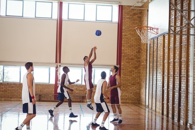 High school basketball players actively participating in a game on an indoor court. Ideal for use in sports-related articles, educational materials, fitness promotions, and teamwork-focused content.