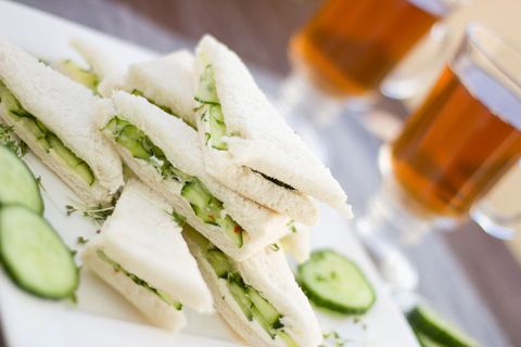 Stacked cucumber tea sandwiches with herb filling and glasses of tea
