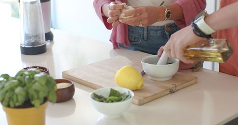 Couple making fresh basil pesto with mortar and pestle in bright kitchen