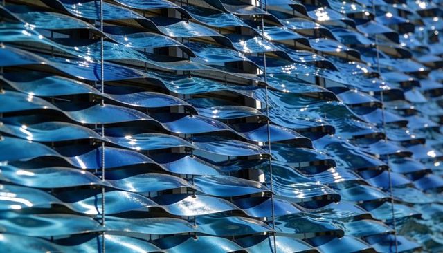 Curved blue louvers forming rippling facade reflecting sunlight on modern building exterior