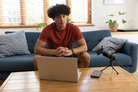 Young Man Recording Podcast at Home on Laptop with Microphone Setup