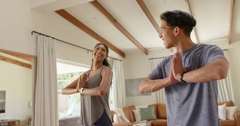 African american couple practicing yoga at home smiling in prayer pose with trackers