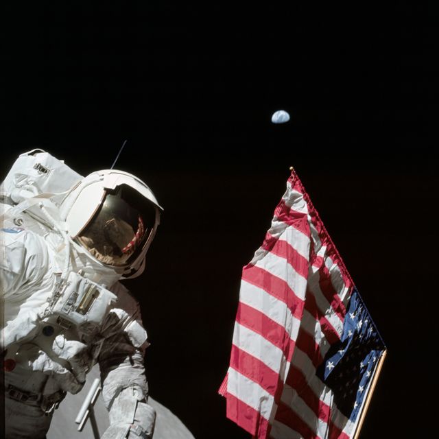 Harrison Schmitt, extraterrestrial geology specialist, proudly stands beside the American flag on the lunar surface as part of the historic Apollo 17 mission. The Earth can be observed in the distant background, highlighting the significant achievement of human space exploration. Great for illustrating achievements in space exploration, human endeavor, and historical moments of the Apollo missions.