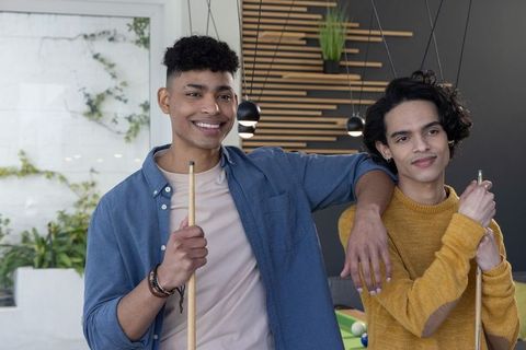 Diverse teenage male friends posing and holding pool cues in modern lounge casual leisure