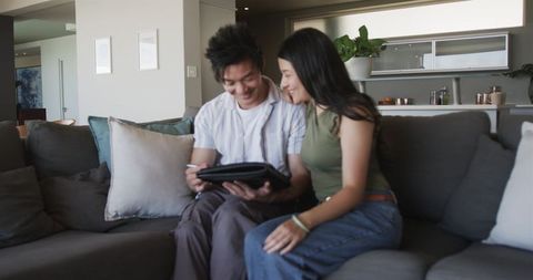 Asian couple sitting on sofa using tablet and stylus in contemporary open-plan living room