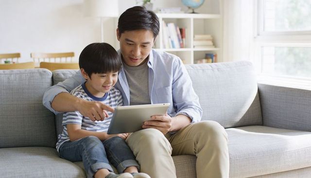 Father and son using tablet on sofa sharing learning, bonding, and family technology moment