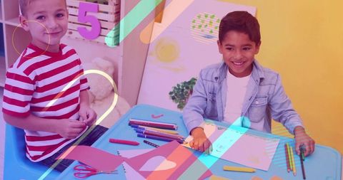 Two Boys Crafting Together at Colorful Classroom Table Using Pencils and Paper