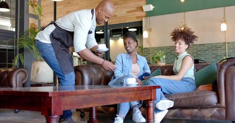 Barista Serving Coffee to Friends Relaxing on Leather Sofa in Trendy Cafe Lounge