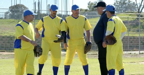 Veteran baseball team huddling with coach on sunlit field in yellow uniforms and blue caps