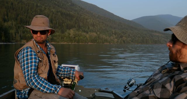 Two men enjoying a quiet fishing trip on a lake surrounded by mountains. Both appear relaxed and engaged in conversation. Ideal for use in promoting outdoor activities, travel destinations, or fishing-related products.